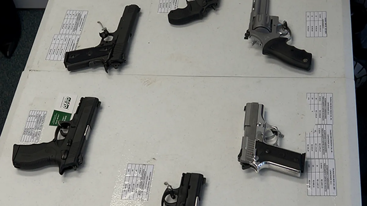 Diversos modelos de pistolas e revólveres dispostos sobre mesa clara ao lado de fichas técnicas