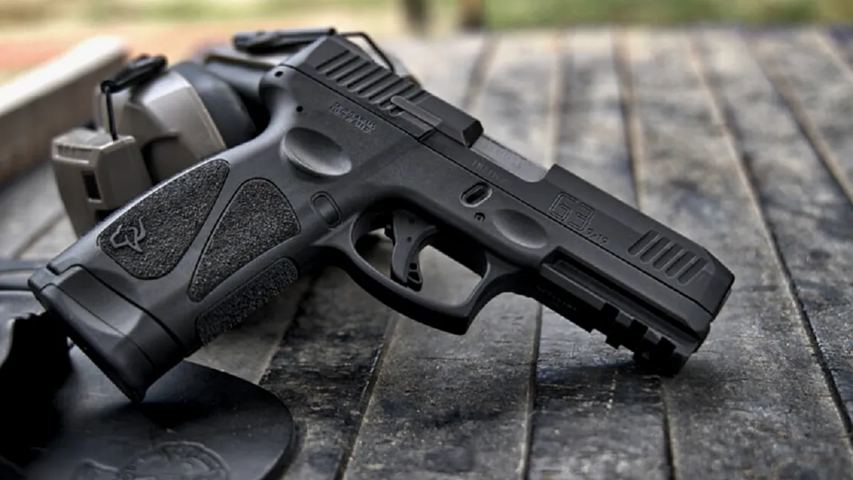 Pistola Taurus sobre bancada de madeira ao lado de protetor auricular, em foto editorial