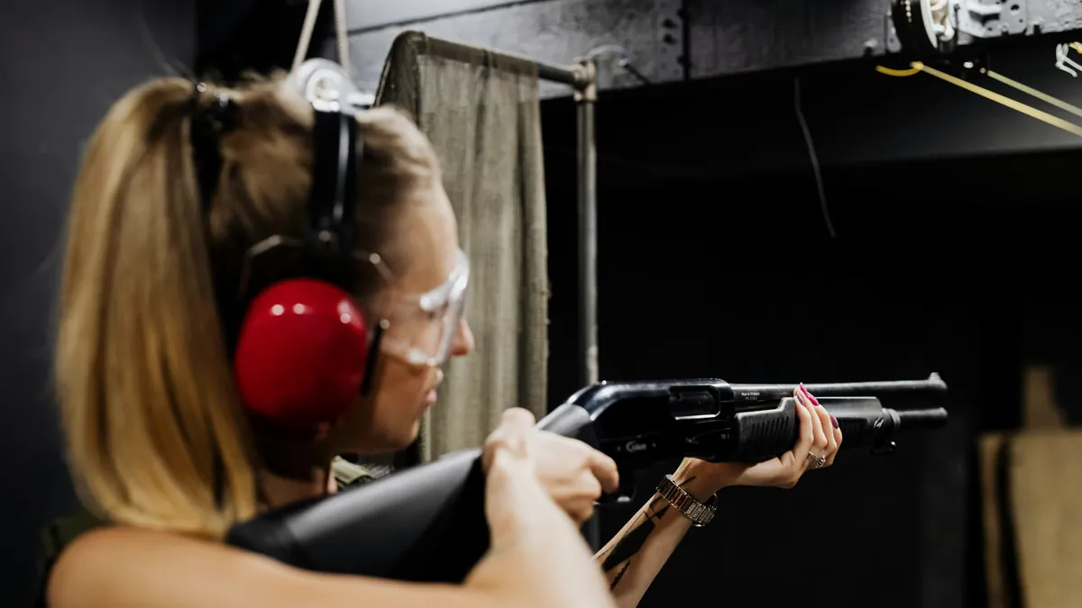 Atiradora esportiva com protetor auricular e óculos de proteção em estande de tiro coberto
